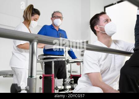 Physiotherapeuten helfen behinderten kaukasischen älteren Mann mit parallelen Bars im Rehabilitationszentrum zu gehen. Hochwertige Fotos Stockfoto