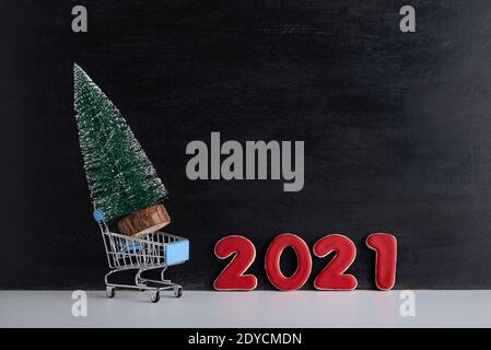 Miniatur-Weihnachtsbaum in Trolley-Wagen vor dem Hintergrund der Inschrift 2021. Kauf und Miete von Weihnachtsbäumen. Stockfoto