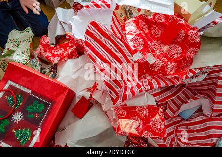 Weggeworfenes Weihnachts-Geschenkpapier, das in einen großen Stapel auf den Boden geworfen wurde und von Geschenken gerissen wurde. Stockfoto