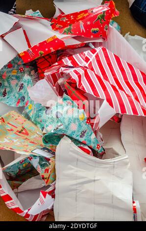 Weggeworfenes Weihnachts-Geschenkpapier, das in einen großen Stapel auf den Boden geworfen wurde und von Geschenken gerissen wurde. Stockfoto