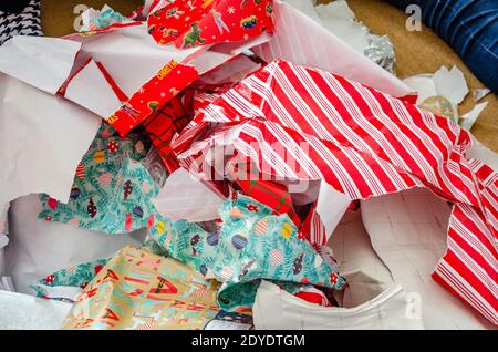 Weggeworfenes Weihnachts-Geschenkpapier, das in einen großen Stapel auf den Boden geworfen wurde und von Geschenken gerissen wurde. Stockfoto