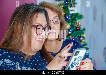 Eine Mutter und ihre Erwachsene Tochter schauen sich in der Weihnachtszeit gemeinsam etwas auf einem Handy an. Stockfoto