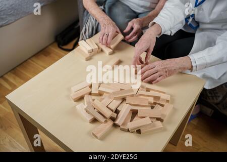 Jenga-Spiel. Thema ist Demenz, Altern und Spiele für alte Menschen. Kaukasische ältere Frau baut Turm aus Holzblöcken mit Hilfe eines Arztes als Teil Stockfoto