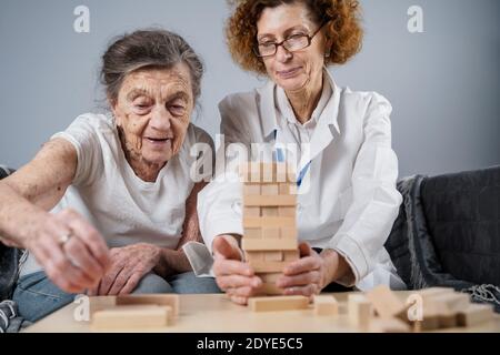 Jenga-Spiel. Thema ist Demenz, Altern und Spiele für alte Menschen. Kaukasische ältere Frau baut Turm aus Holzblöcken mit Hilfe eines Arztes als Teil Stockfoto