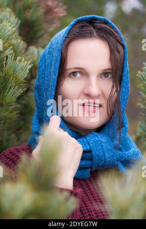 Portrait der Brünette Frau mit langen Haaren und braunen Augen im Kiefernwald stehen. Hübsche junge Frau in braunem Strickpullover und blauem Schal gekleidet Stockfoto