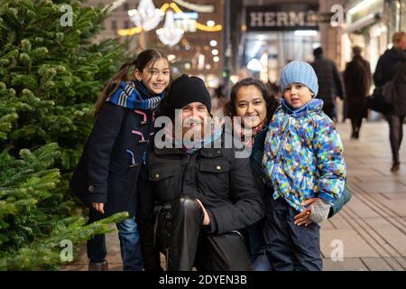 Glückliche multinationale Familie mit Mama, Papa und Kindern im Freien in einem Stadtzentrum zur Weihnachtszeit. In die Kamera Stockfoto