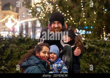 Glückliche multinationale Familie mit Mama, Papa und Kindern, die Spaß im Freien in einem wunderschön dekorierten Stadtzentrum zu Weihnachten haben Stockfoto