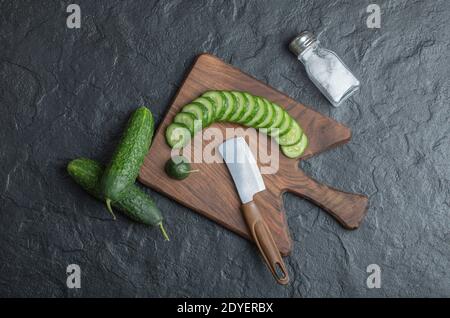 In Scheiben oder ganze Gurke auf Holzbrett mit Salz und Messer Stockfoto