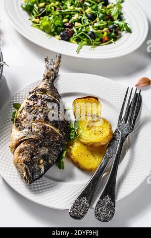 Abendessen mit gegrilltem Fisch aus der Meeresbrasse, Rucola-Salat mit Tomaten, gebackene Kartoffeln. Weißer Hintergrund. Draufsicht Stockfoto