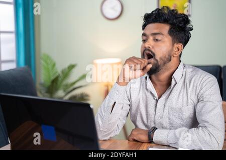 Junger Mann wurde müde und gähnend während der Arbeit auf Laptop zu Hause - Konzept schlaflose Arbeit, Müdigkeit und erschöpft IT-Berufsjob während der Arbeit aus Stockfoto