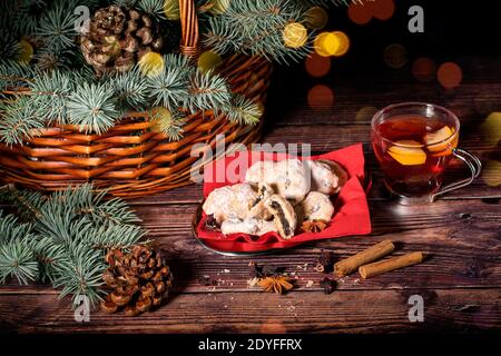 Kekse mit Mohnsamen, Korb voller Zweige der Blautanne, Kiefern und Tasse Tee auf dem Holzhintergrund. Weihnachts- und Neujahrskonzept, lig Stockfoto