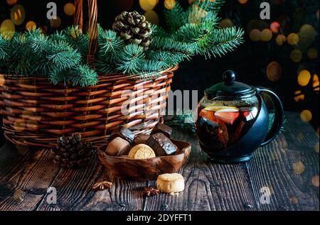 Hausgemachte verschiedene Kekse in der Holzplatte, Korb voller Zweige der blauen Tanne, Teekanne auf dem dekorierten Küchentisch. Weihnachten und Neujahr conce Stockfoto