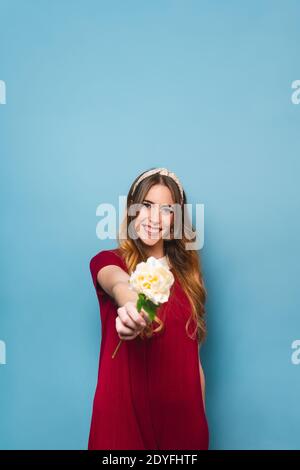 Nette junge Frau, die eine rwhite Rose gegen einen bue hält Hintergrund Stockfoto