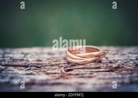 Nahaufnahme eines Rings mit drei Ringen auf Holzhintergrund. Hochzeitsschmuck in Gold, Weißgold und Roségold. Makroaufnahme mit selektivem Fokus und Kopie Stockfoto