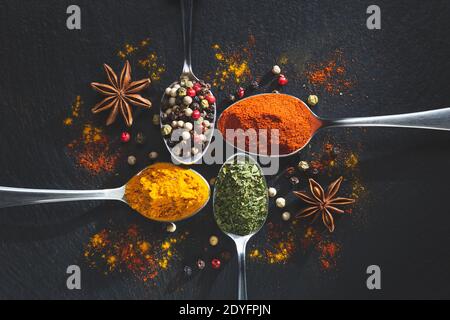 sternanis und Löffel mit Pfeffer, Paprika, Petersilie und Kurkuma auf schwarzem Hintergrund mit Kopierraum, Draufsicht. Kochen Zutaten und Condiments Konz Stockfoto