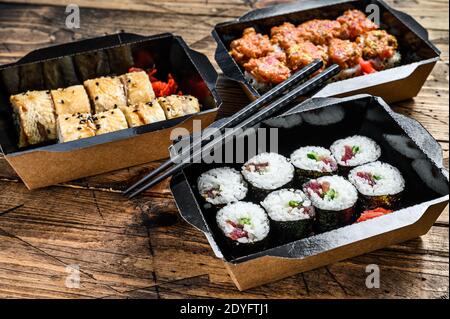 Die Sushi-Rollen im Lieferpaket, bestellt im Sushi-Take-Out-Restaurant. Holzhintergrund. Draufsicht Stockfoto