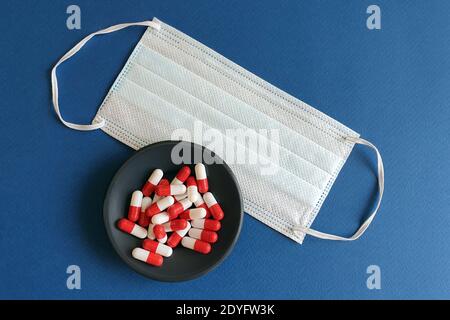 Medikamente und Schutzmasken. Neuartiges Coronavirus 2019-nCoV, MERS-Cov Mitte. Medizinische Pillen auf einem schwarzen Teller und medizinische Maske. Blauer Hintergrund. Aushärten f Stockfoto