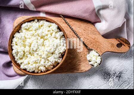 Frischer Hüttenkäse in einer Holzschüssel auf Schneidebrett. Grauer Hintergrund. Draufsicht Stockfoto