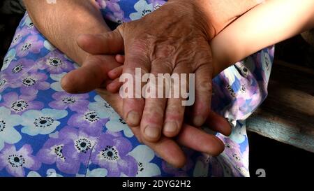 Alte Dame und Kleinkind Hände Nahaufnahme. Urgroßmutter hält kleine Hand ihres Urenkindes zwischen ihre alten faltigen Handflächen. Verschiedene Hände von Stockfoto