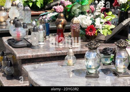 Kerzen, viele Votivlichter und Blumen, Dekoration auf einem Grab Nahaufnahme. Lichter an der Friedhofsdetailaufnahme, aus nächster Nähe Tod, Erinnerung, Vergehen Stockfoto