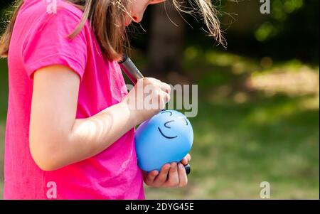 Kleines Kind, sa kleines Mädchen Zeichnung ein glücklich lächelndes Gesicht auf einem Ballon mit einem schwarzen Marker im Freien, Nahaufnahme. Kinder und imaginäre Freunde Einsamkeit Stockfoto