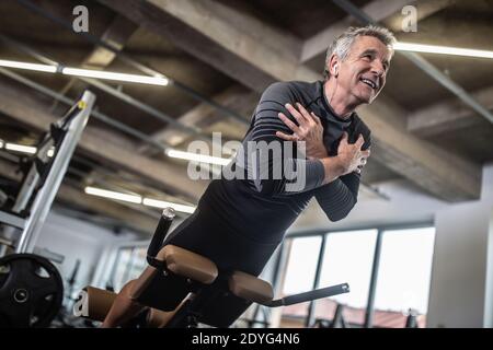 Übung des unteren Rückens durch einen älteren Mann in einem industriell aussehenden Fitnessstudio. Stockfoto