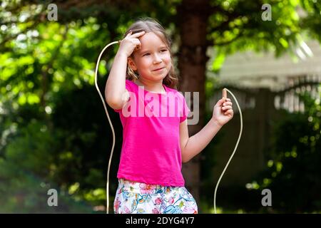 Ein glückliches kleines Mädchen, Kind mit einem Springseil im Garten draußen, Kind hält ein Springseil lächelnd im Freien, Nahaufnahme, Portrait Sport Stockfoto