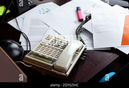 Chaos auf einem Schreibtisch, Telefon, viele Papiere und Firmendokumente, einfache chaotische Arbeitsplatz, viele überwältigende Arbeitsszene Stockfoto