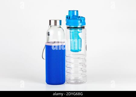 Zwei leere Sportreisewasserflaschen auf weiß, eine Plastikflasche mit Fruchtauffüllung, eine Glasflasche. Paar stilvolle Trinkwasserbehälter, Hydratation Stockfoto