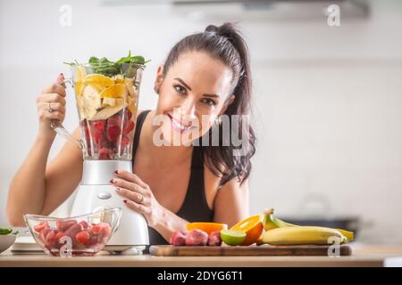 Schönes Mädchen hält Mixer voll von gesunden Sachen vor dem Mischen in ein gesundes Frühstück. Stockfoto