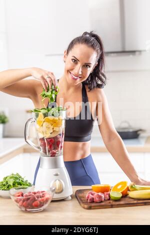 Post-Workout Ernährung für eine Frau in Fitness-Kleidung in Form von roten Beeren, Orangen und Spinat in einem Mixer. Stockfoto