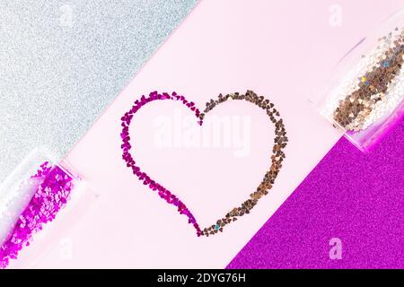Herzform aus mehrfarbigem Glitzer. Zwei Sektgläser mit herzförmigem Konfetti auf Glitzerhintergrund. Valentinstag-Konzept. Stockfoto