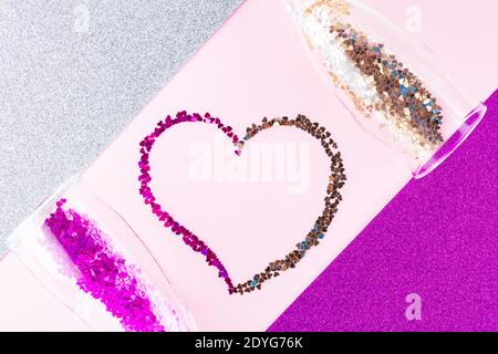 Herzform aus mehrfarbigem Glitzer. Zwei Sektgläser mit herzförmigem Konfetti auf Glitzerhintergrund. Valentinstag-Konzept. Stockfoto
