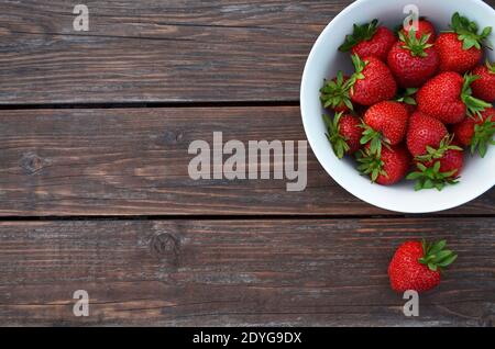 Frische rote Erdbeeren in einer weißen Schüssel auf einem alten Holztisch Nahaufnahme mit Kopierplatz, Draufsicht. Gesunde Ernährung Konzept. Stockfoto