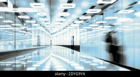 Verschwommene Silhouette eines Geschäftsreisenden, der durch die modern beleuchtete Flughafenterminal-Halle läuft. Stockfoto