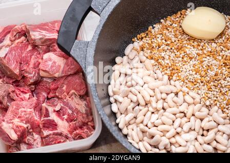 Nahaufnahme des traditionellen jüdischen Cholent Hamin - Hauptgericht für die Schabbat Mahlzeit langsam gekochtes Rindfleisch mit Kartoffeln, Bohnen, Weizenkörnern und Gewürzen in einer Kasserolle auf einem grauen Marmor Küchentisch. Stockfoto