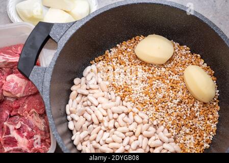 Nahaufnahme des traditionellen jüdischen Cholent Hamin - Hauptgericht für den Schabbat. Rohes Rindfleisch wird einem Topf mit Kartoffeln, Zwiebeln, Bohnen und Weizenkörnern hinzugefügt Stockfoto