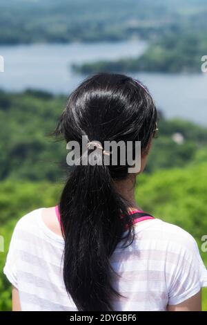 Eine chinesische Frau mit schwarzen Haaren, die von der Spitze des Pinnacle auf dem Macricostas Preserve in New Preston Connecticut über den Lake Waramaug blickt. Stockfoto