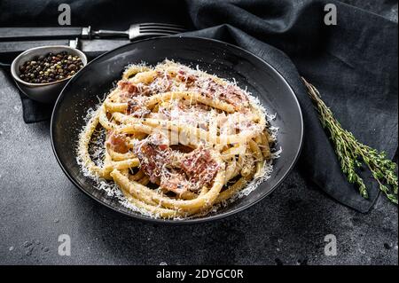 Pasta Carbonara auf schwarzem Teller mit Parmesan, Bucatini. Schwarzer Hintergrund. Draufsicht Stockfoto