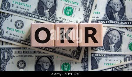 OKR-Symbol. Konzeptworte 'OKR - Ziele und Schlüsselergebnisse' auf Holzwürfeln auf einem schönen Hintergrund aus Dollarscheinen. Business und OKR – Ziel Stockfoto