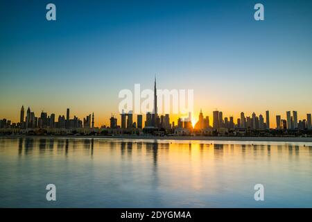 Sonnenaufgang in Dubai mit klarem blauen Himmel Blick vom Boot oder Meer. Morgens geht die Sonne über den Wolkenkratzern der VAE auf. Dubai Strand, Küste, Ufer Stockfoto