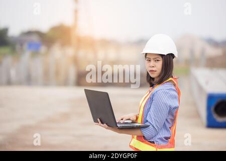 Schöne asiatische weibliche Ingenieur in weißen Sicherheit Hut mit Laptop-Computer Notebook Arbeit auf Baustelle außerhalb Büro. Idee für modern Stockfoto