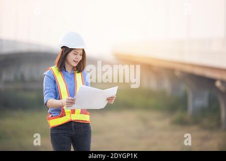Schöne asiatische weibliche Ingenieur in weiß Sicherheit Hut tun Arbeit auf Baustelle außerhalb Büro. Idee für moderne arbeitende Frau Hightway Straße Stockfoto