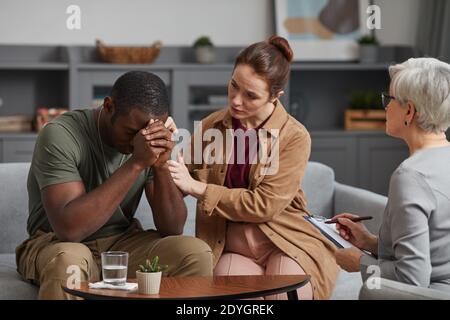 Junge Frau unterstützt deprimierten afrikanischen Mann, während sie Psychologen besuchen Stockfoto