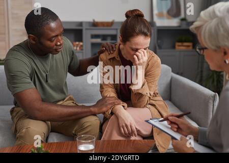 Junge depressive Frau besucht Psychologe zusammen mit jungen Mann, der Unterstützt sie Stockfoto