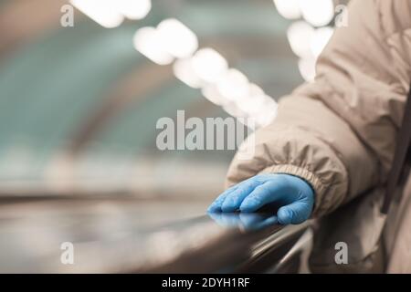 Nahaufnahme einer Frau in Schutzhandschuhen, die auf der Rolltreppe steht Unterirdisch Stockfoto