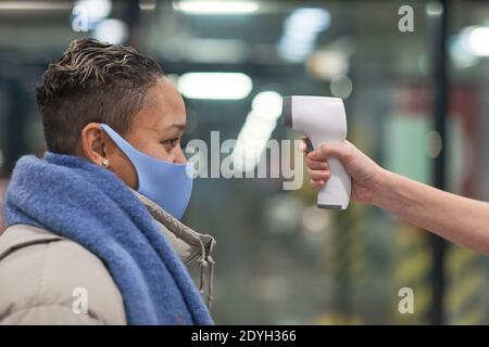 Seitenansicht der Frau in Schutzmaske, die ihre Temperatur überprüft Vor dem Betreten im Supermarkt Stockfoto