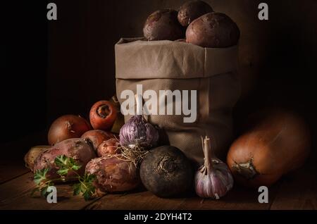 Kartoffeln in einem Stoffbeutel und anderes Gemüse in einem Rustikaler Stil auf einem dunklen Holzhintergrund Stockfoto