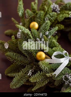 Wunderschön grüner Weihnachtskranz mit goldenen Kugeln auf dunkler Holzfläche, 45 Grad Winkel, satte Farben Stockfoto