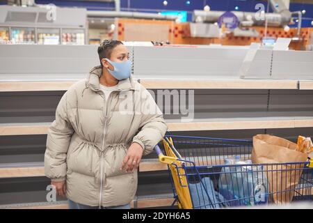Junge Frau in Schutzmaske stehend mit Warenkorb in Supermarkt und Einkaufen Stockfoto